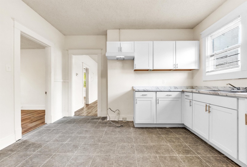Kitchen featuring baseboards, light stone counters, light tile patterned floors, white cabinetry, and a sink