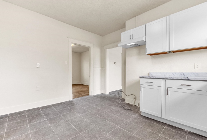 Kitchen featuring tile patterned floors, white cabinetry, baseboards, and light stone countertops