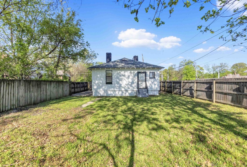 Rear view of property featuring a yard, a fenced backyard, and a chimney