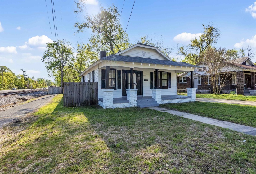 Bungalow with a chimney, covered porch, fence, and a front lawn