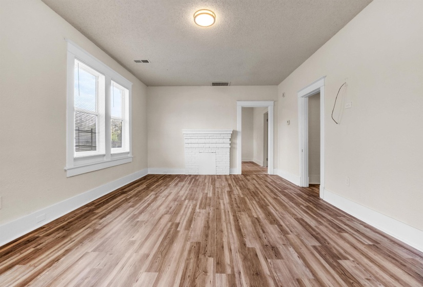 Unfurnished living room featuring visible vents, baseboards, wood finished floors, and a textured ceiling