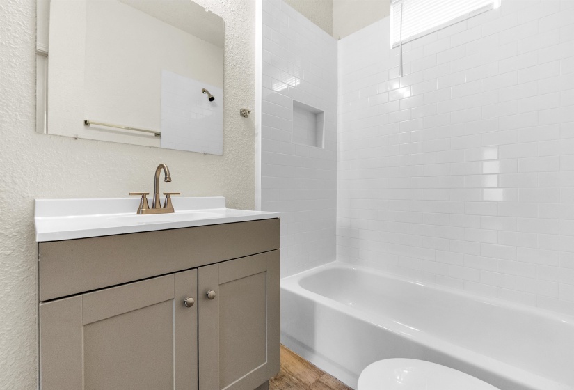 Bathroom featuring a textured wall, bathing tub / shower combination, vanity, and toilet