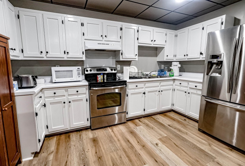 Kitchen with under cabinet range hood, appliances with stainless steel finishes, light wood-style flooring, and light countertops