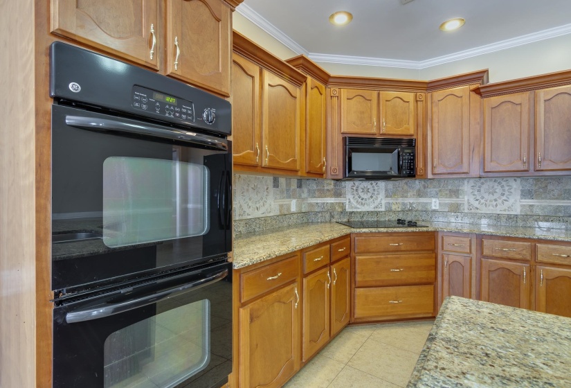 Kitchen featuring black appliances, backsplash, light stone counters, crown molding, and brown cabinets