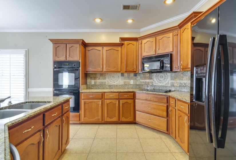 Kitchen with ornamental molding, black appliances, tasteful backsplash, light stone countertops, and light tile patterned floors