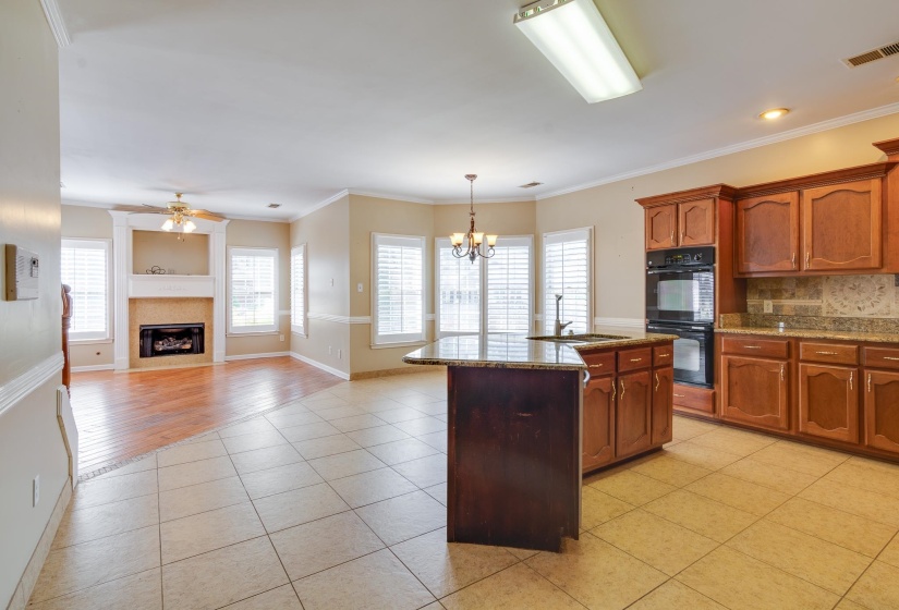 Kitchen featuring crown molding, dark stone countertops, tasteful backsplash, a center island with sink, and pendant lighting