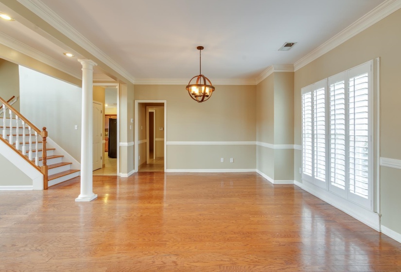 Unfurnished room featuring crown molding, light wood-style flooring, a chandelier, stairs, and ornate columns