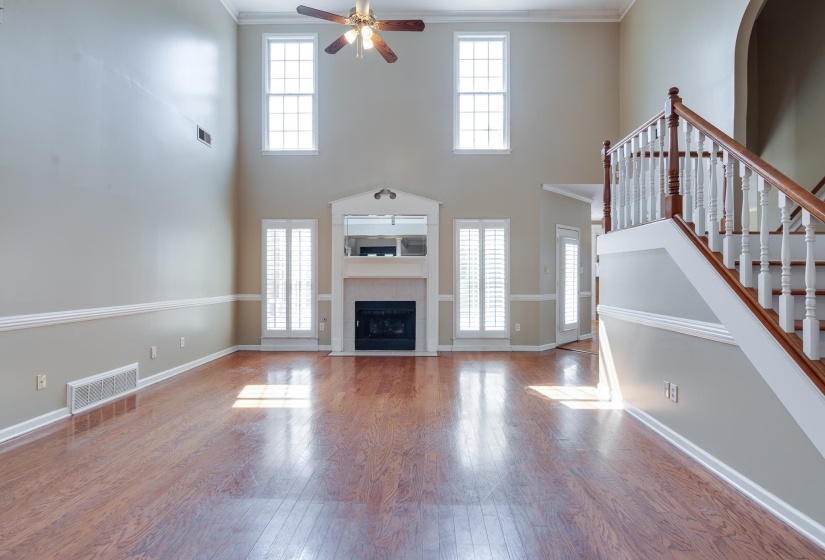 Unfurnished living room featuring healthy amount of natural light, wood-type flooring, a towering ceiling, stairs, and crown molding