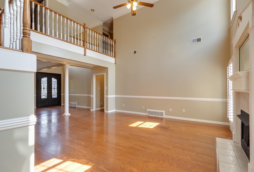 Unfurnished living room featuring light wood-style floors, a tiled fireplace, ornamental molding, a high ceiling, and french doors