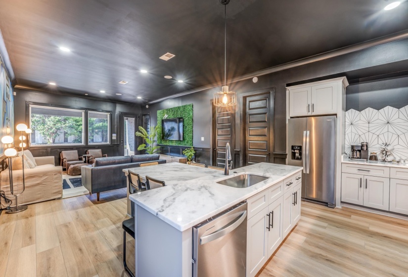 Kitchen with stainless steel appliances, a sink, open floor plan, light wood-style floors, and light stone countertops