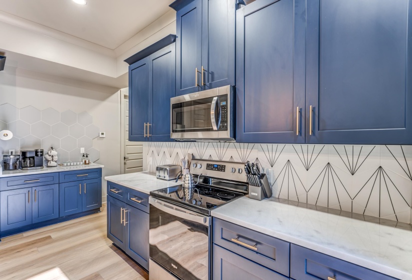 Kitchen with blue cabinets, light wood-type flooring, appliances with stainless steel finishes, and tasteful backsplash