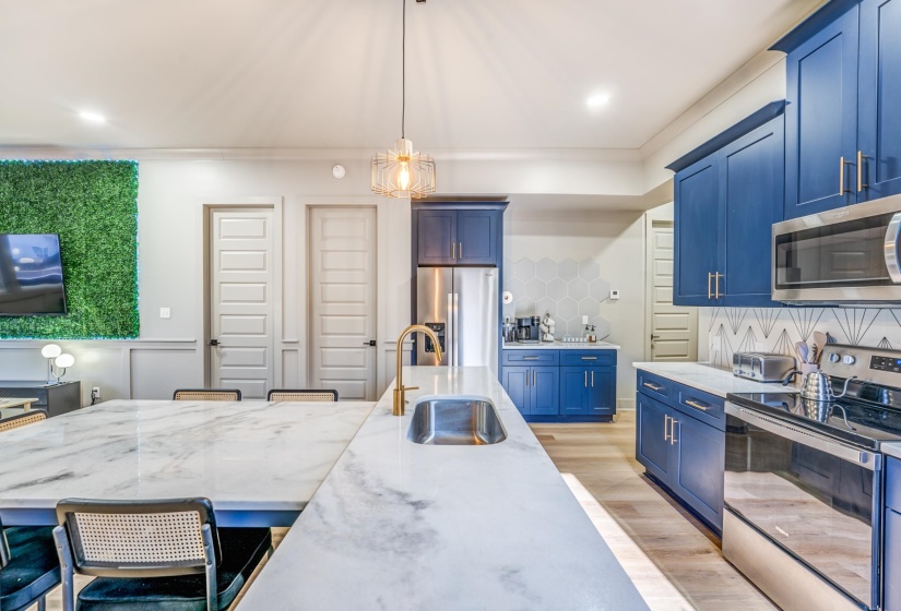 Kitchen featuring light wood finished floors, blue cabinets, a sink, tasteful backsplash, and appliances with stainless steel finishes