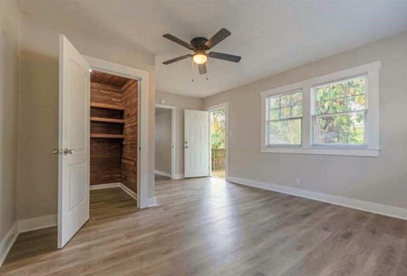 Unfurnished bedroom with a walk in closet, ceiling fan, wood walls, and light hardwood / wood-style flooring