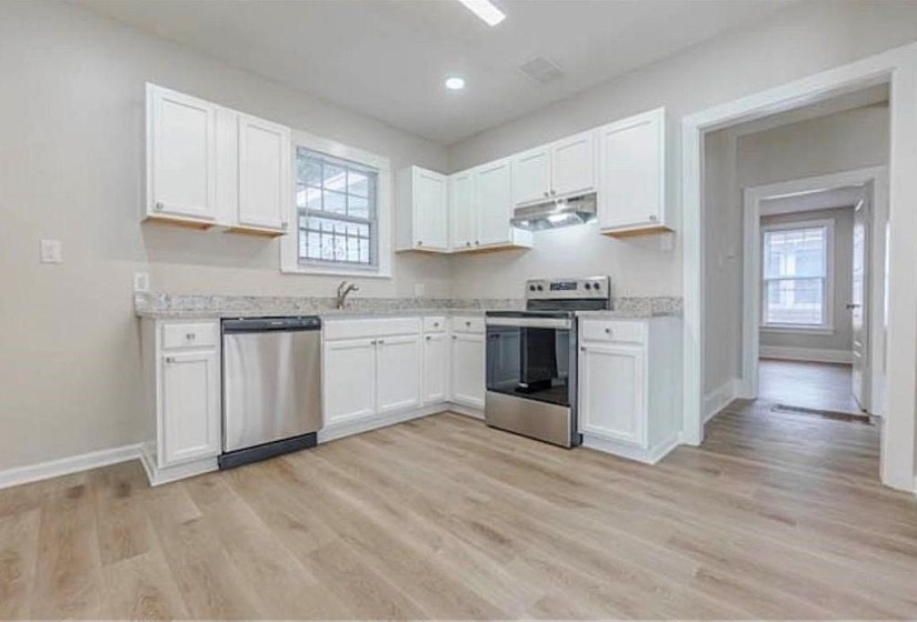 Kitchen with light hardwood / wood-style floors, white cabinets, appliances with stainless steel finishes, and a healthy amount of sunlight