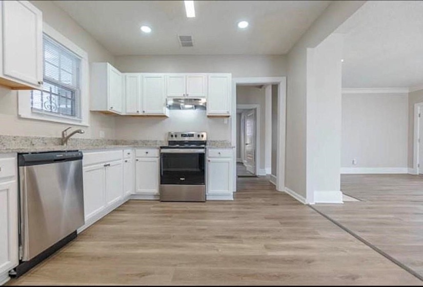 Kitchen with light stone counters, light hardwood / wood-style floors, crown molding, white cabinetry, and appliances with stainless steel finishes