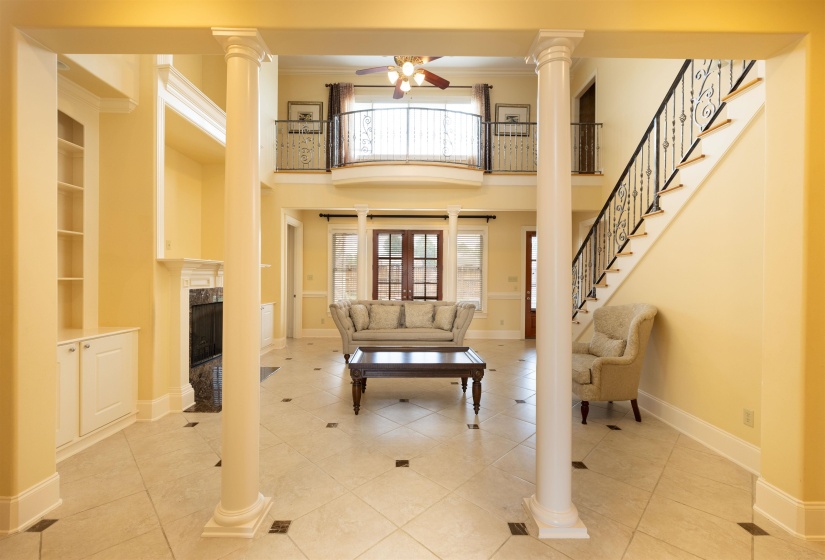 Foyer featuring a ceiling fan, a premium fireplace, crown molding, ornate columns, and tile patterned floors
