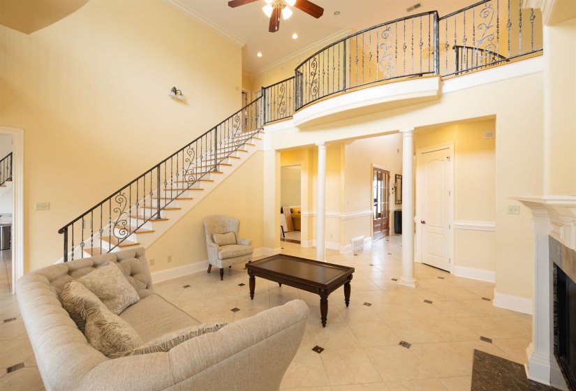 Living room with a high ceiling, decorative columns, ceiling fan, stairway, and tile patterned floors
