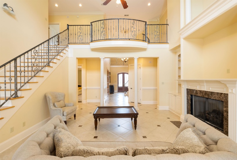 Living area featuring ornate columns, ornamental molding, stairway, a towering ceiling, and a ceiling fan