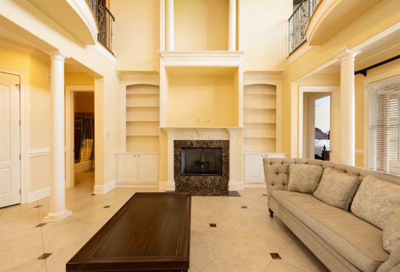 Living area featuring ornate columns, a high ceiling, built in shelves, light tile patterned floors, and a fireplace