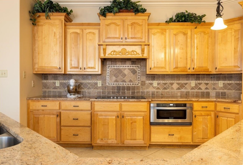 Kitchen featuring stainless steel oven, decorative backsplash, light stone countertops, and hanging light fixtures