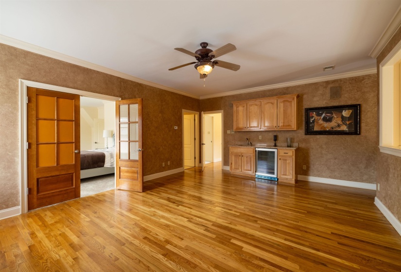 Unfurnished living room with light wood-type flooring, wine cooler, a ceiling fan, crown molding, and bar