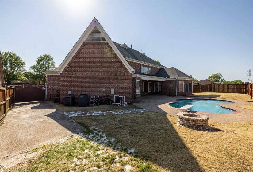 Back of house with a fenced in pool, a fenced backyard, a fire pit, brick siding, and a yard