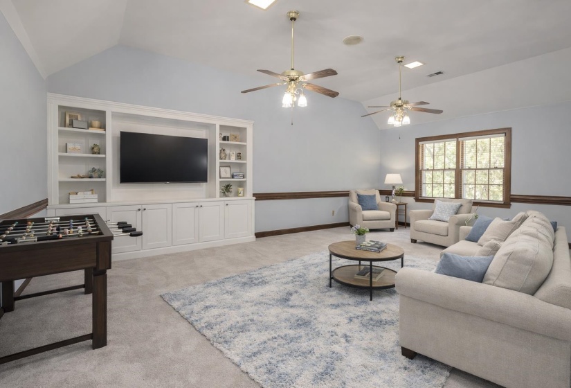 Living area with built in shelves, light colored carpet, and a ceiling fan