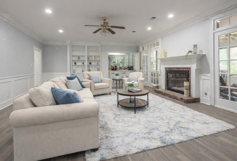 Living area with a decorative wall, wainscoting, wood finished floors, ceiling fan, and crown molding