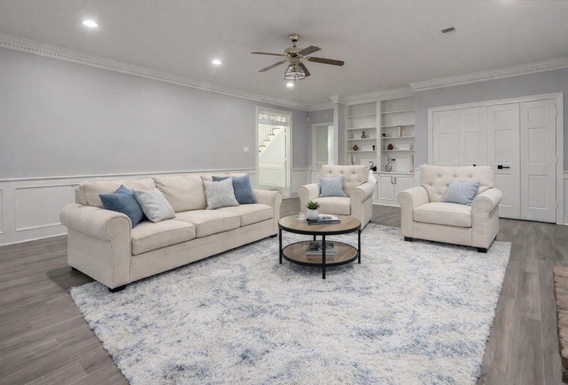 Living room with ornamental molding, ceiling fan, wood finished floors, a wainscoted wall, and a decorative wall