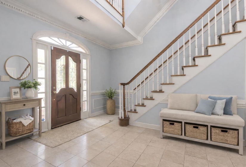 Entrance foyer featuring crown molding, a decorative wall, light tile patterned floors, and wainscoting