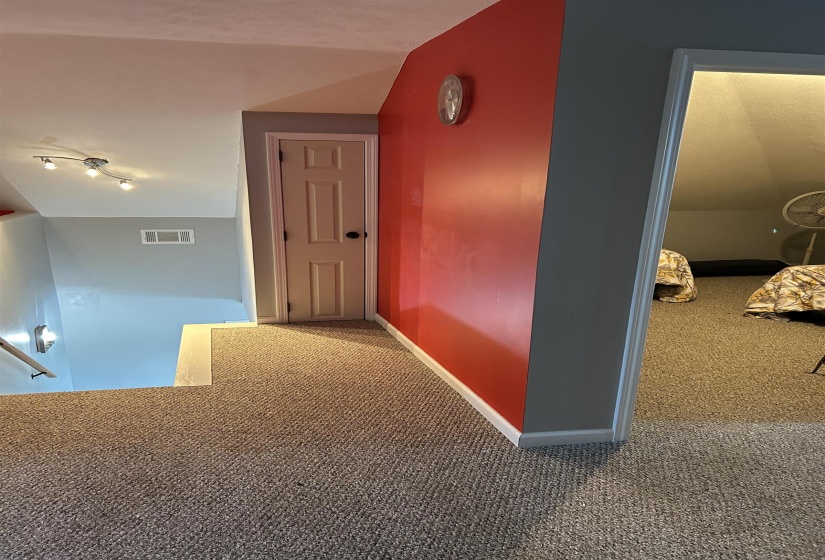 Hallway featuring carpet, visible vents, baseboards, and an upstairs landing Hallway featuring carpet, visible vents, baseboards, and an upstairs landing