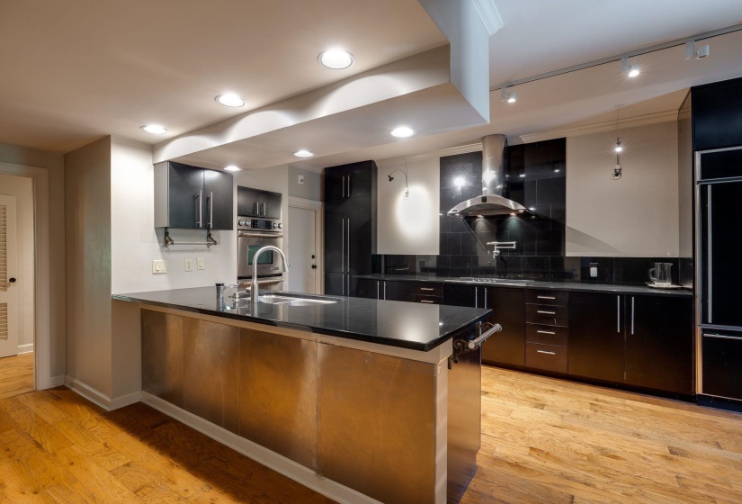 Kitchen with exhaust hood, a sink, dark countertops, decorative backsplash, and hardwood floors