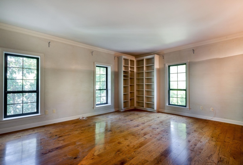 Primary Bedroom with healthy amount of natural light, hardwood floors, baseboards, and crown molding