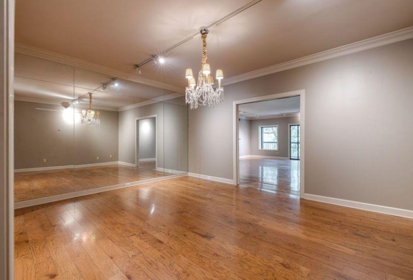 Empty room with a chandelier, crown molding, rail lighting, wood finished floors, and baseboards