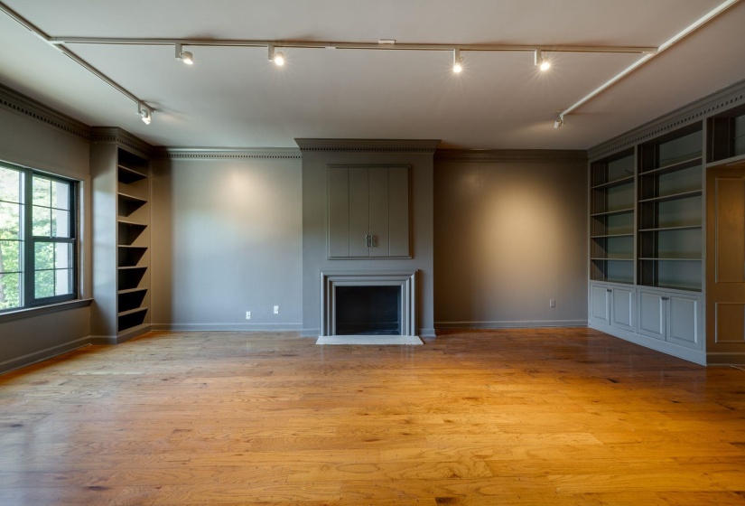 Unfurnished den with track lighting, built in shelves, a large fireplace, and ornamental molding