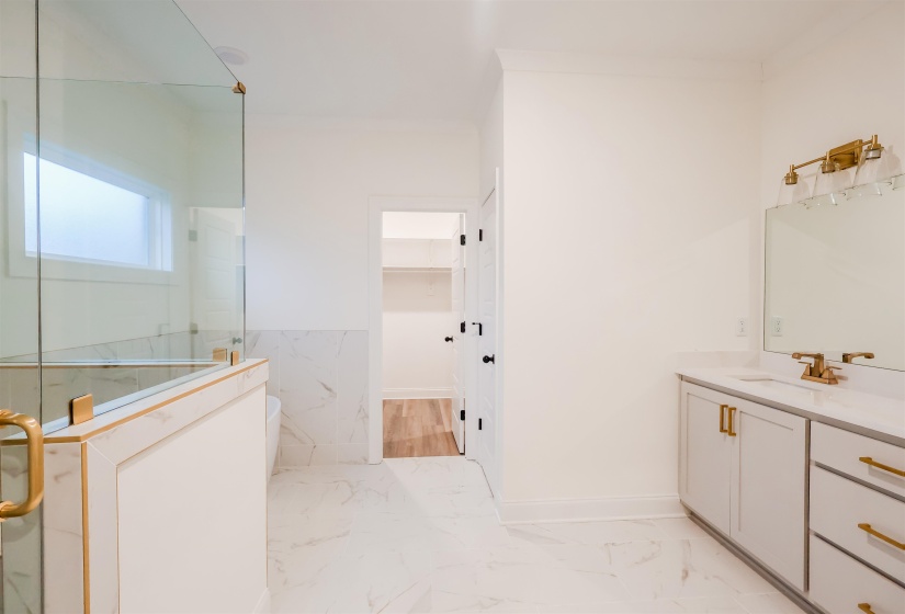 Full bathroom with a walk in closet, a marble finish shower, vanity, light marble finish flooring, and a wainscoted wall