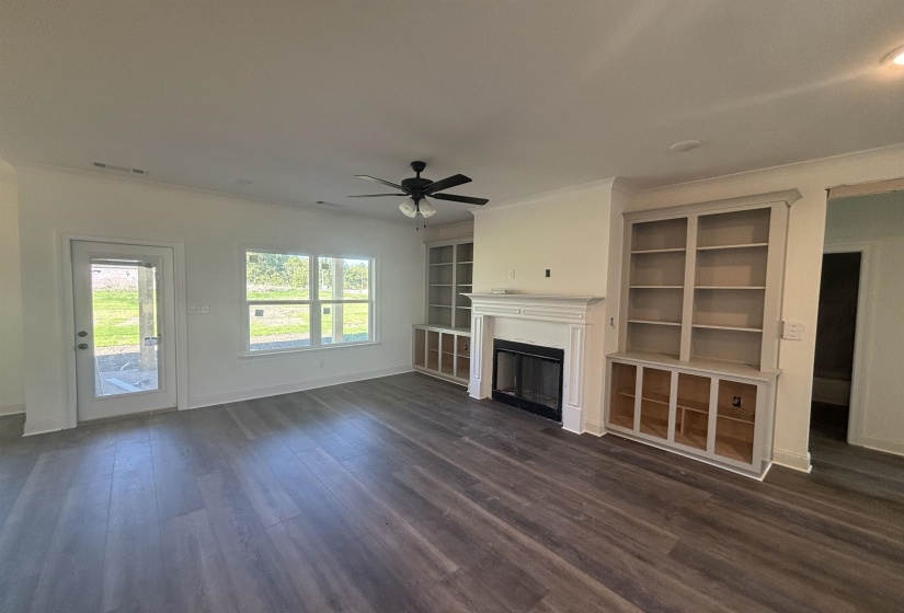 Unfurnished living room featuring a fireplace, dark wood finished floors, built in features, and ceiling fan