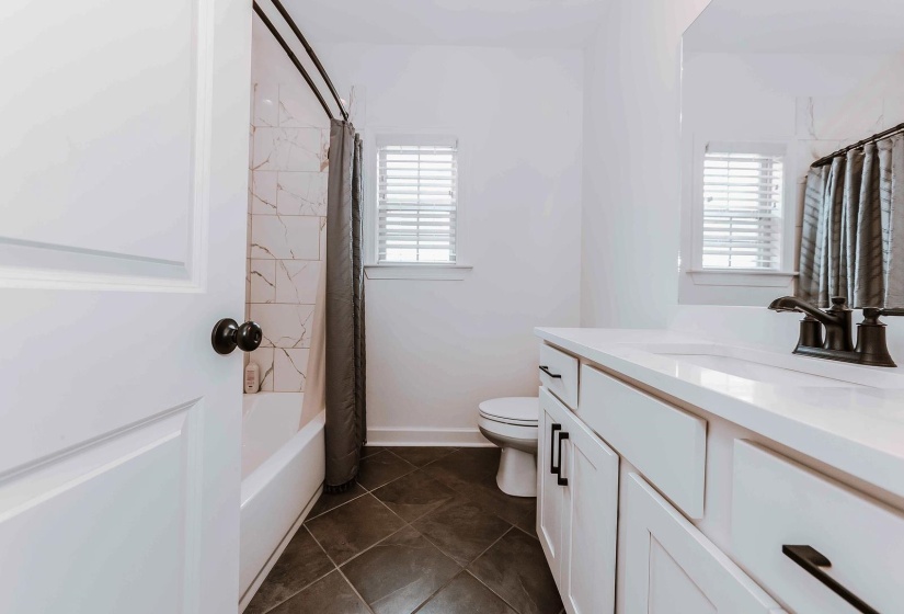 Bathroom with tile patterned flooring, vanity, toilet, baseboards, and shower / tub combo