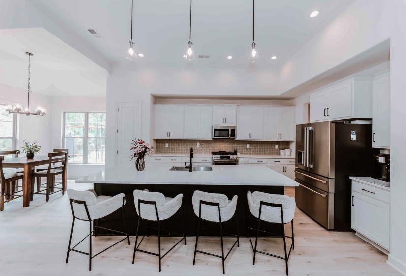 Kitchen with a kitchen bar, tasteful backsplash, light countertops, premium appliances, and white cabinetry