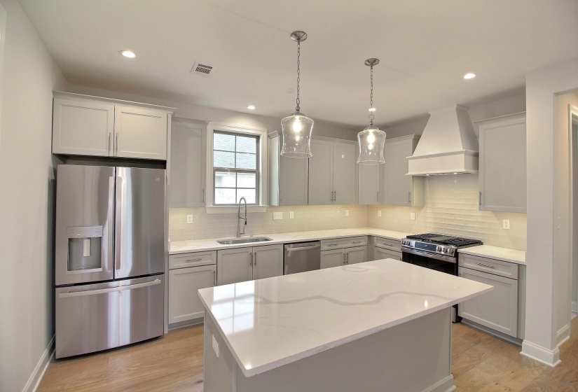 Kitchen with light stone countertops, sink, stainless steel appliances, a kitchen island, and custom exhaust hood
