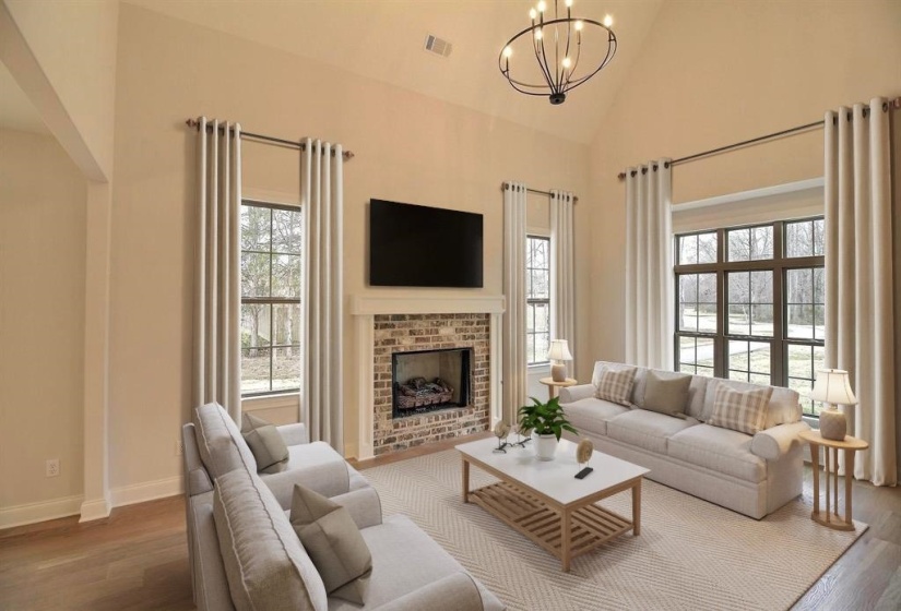 Living room featuring wood finished floors, high vaulted ceiling, a brick fireplace, and a chandelier