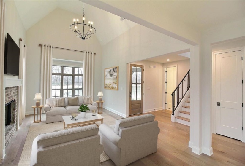 Living area featuring light wood-style floors, healthy amount of natural light, stairs, high vaulted ceiling, and a brick fireplace