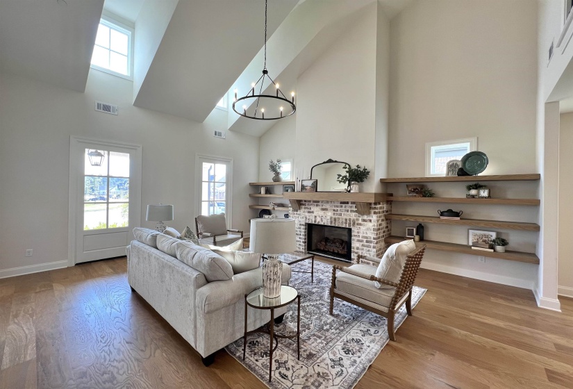 Living room featuring high vaulted ceiling, a chandelier, light wood finished floors, a fireplace, and healthy amount of natural light