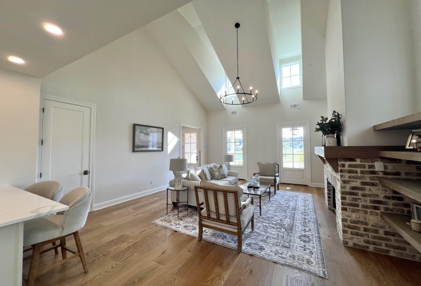 Living room featuring high vaulted ceiling, a chandelier, light wood-style flooring, and a brick fireplace