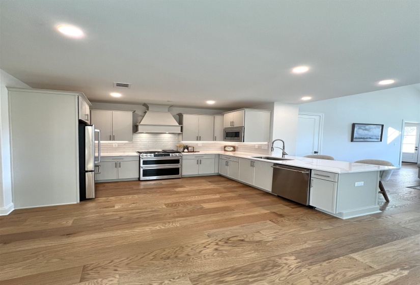 Kitchen featuring premium range hood, a peninsula, stainless steel appliances, tasteful backsplash, and a breakfast bar