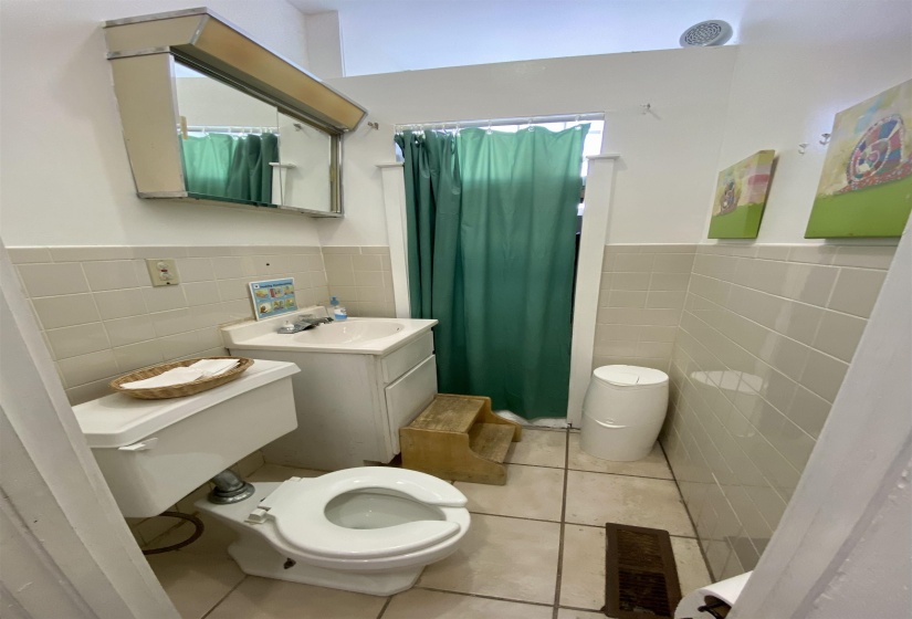 Bathroom with tile patterned flooring, wainscoting, toilet, and tile walls