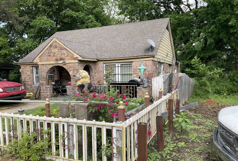 View of front facade with fence, a shingled roof, and stone siding