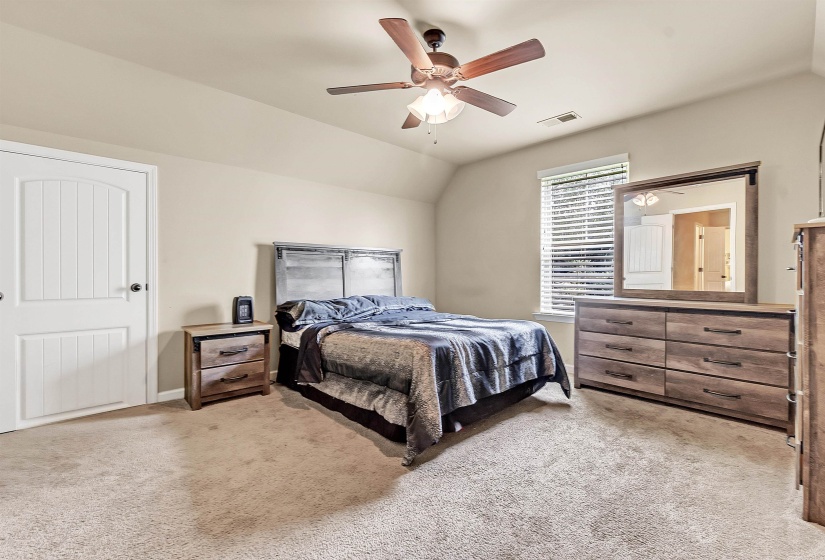 Bedroom with light colored carpet, a ceiling fan, visible vents, and lofted ceiling