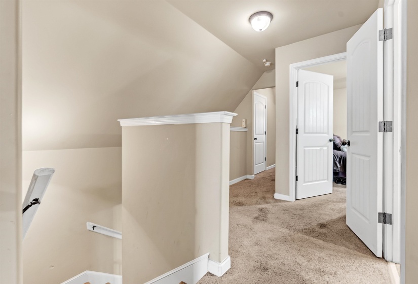 Hallway featuring vaulted ceiling, light carpet, an upstairs landing, and baseboards
