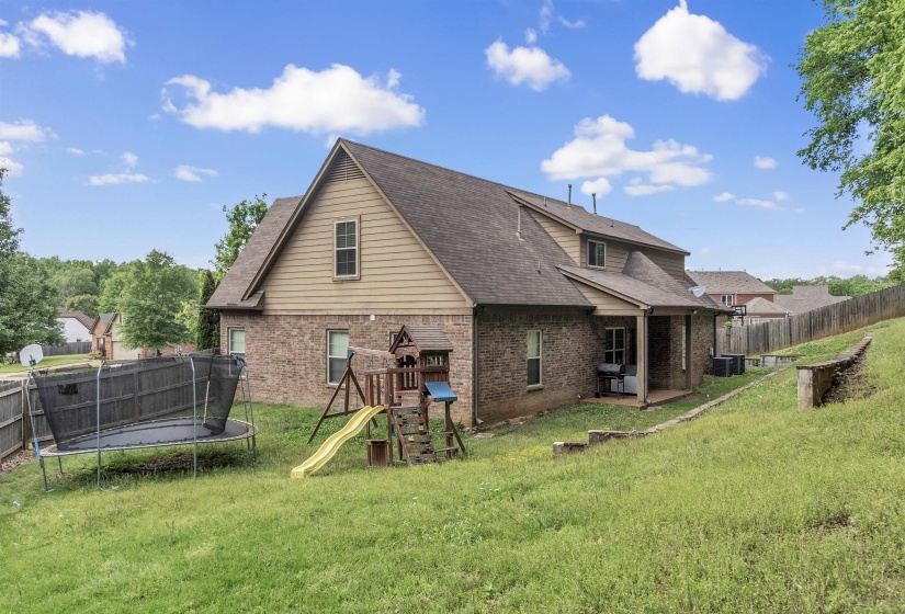 Back of house featuring a lawn, a trampoline, brick siding, and a playground